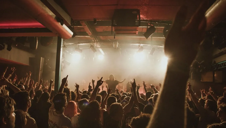 Energetic crowd cheering with hands raised at a live concert performance under bright stage lights at The Governor Hindmarsh (The Gov) in Adelaide.